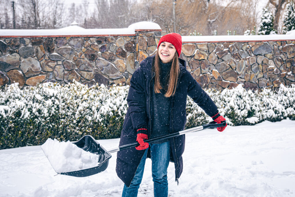 Young woman cleans snow in the yard in snowy weather.